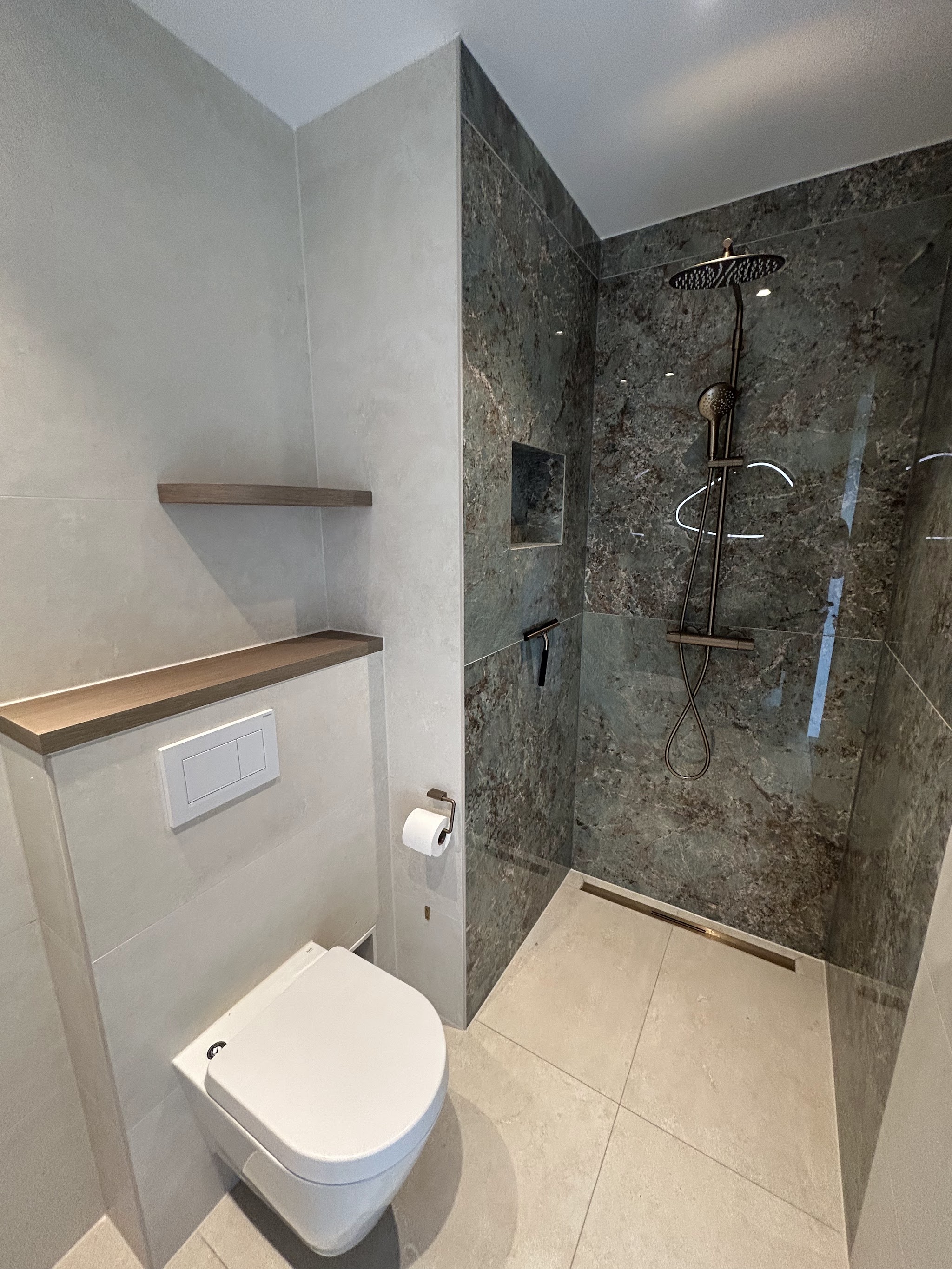 Inloopdouche met donkere marmerlook wand, nis, regendouche en lijngoot naast een hangend toilet